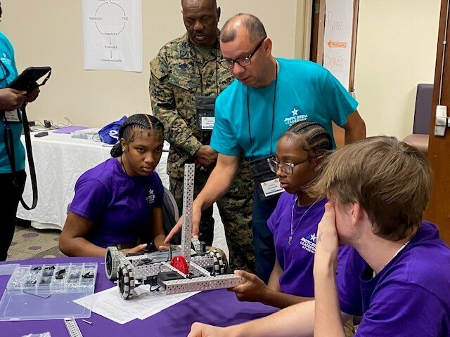 Two instructors and three students work on a clawbot