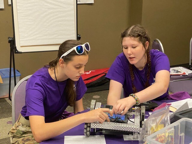 Two JROTC cadets in purple shirts working on a robot