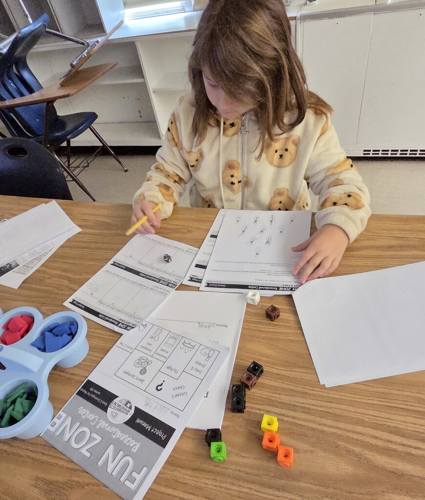 A student sitting at a table works with a worksheet and several dice of different colors