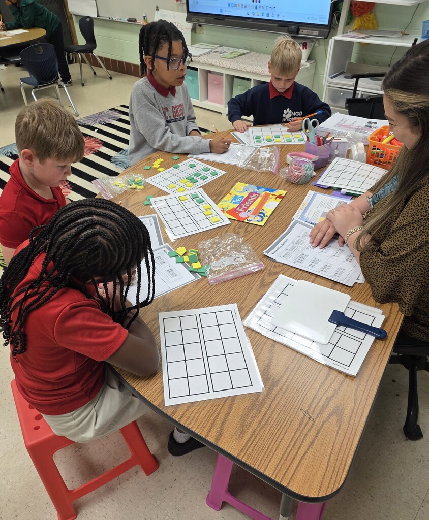 Students around a table work with math manipulatives while a teacher looks on
