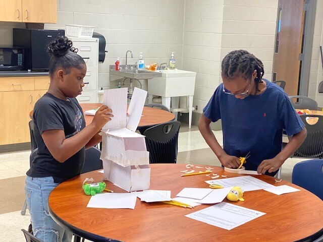 Two girls construct a tower made of paper