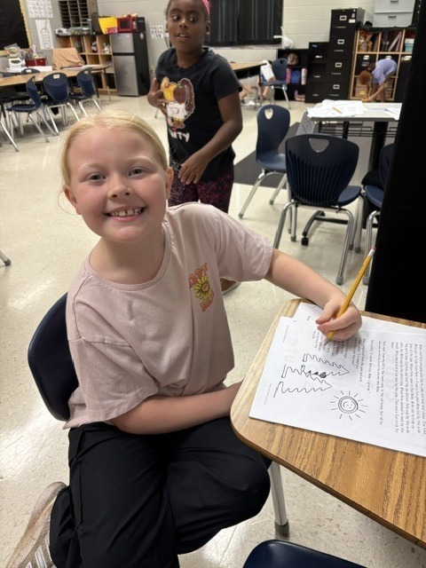 A smiling student does a worksheet at her desk