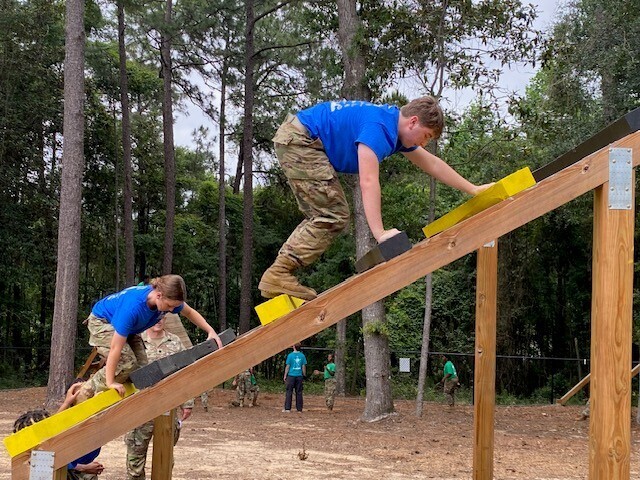 Two JROTC cadets climb up a wooden tower
