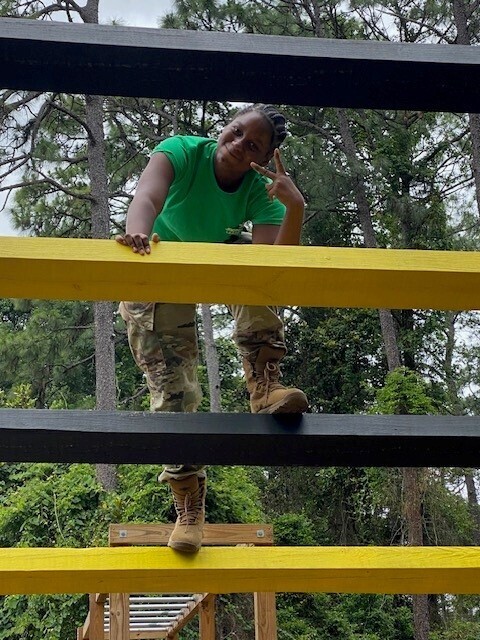A JROTC cadet flashes the peace sign while climbing over an obstacle