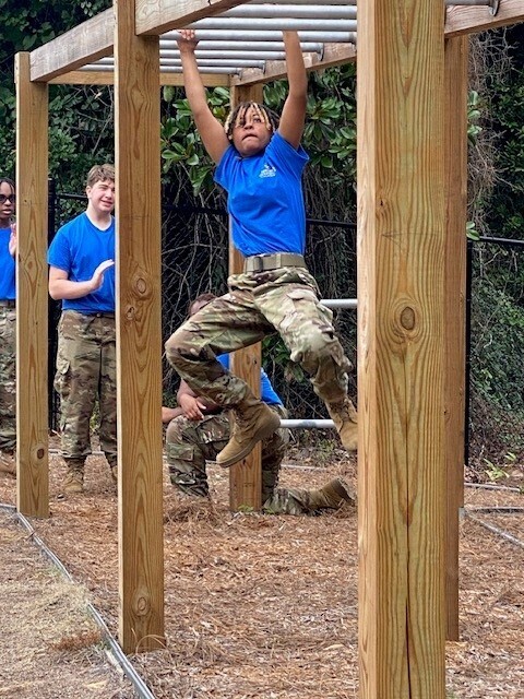 A JROTC cadet swings on a set of monkey bars