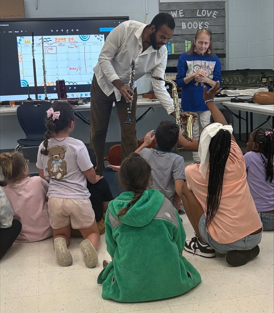 A man lets students touch a small saxophone