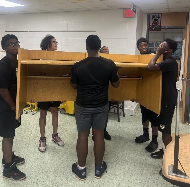 Williamson football players carrying a large desk