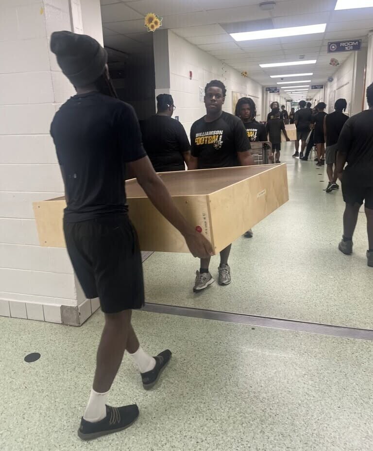 Williamson football players carry furniture down a hallway
