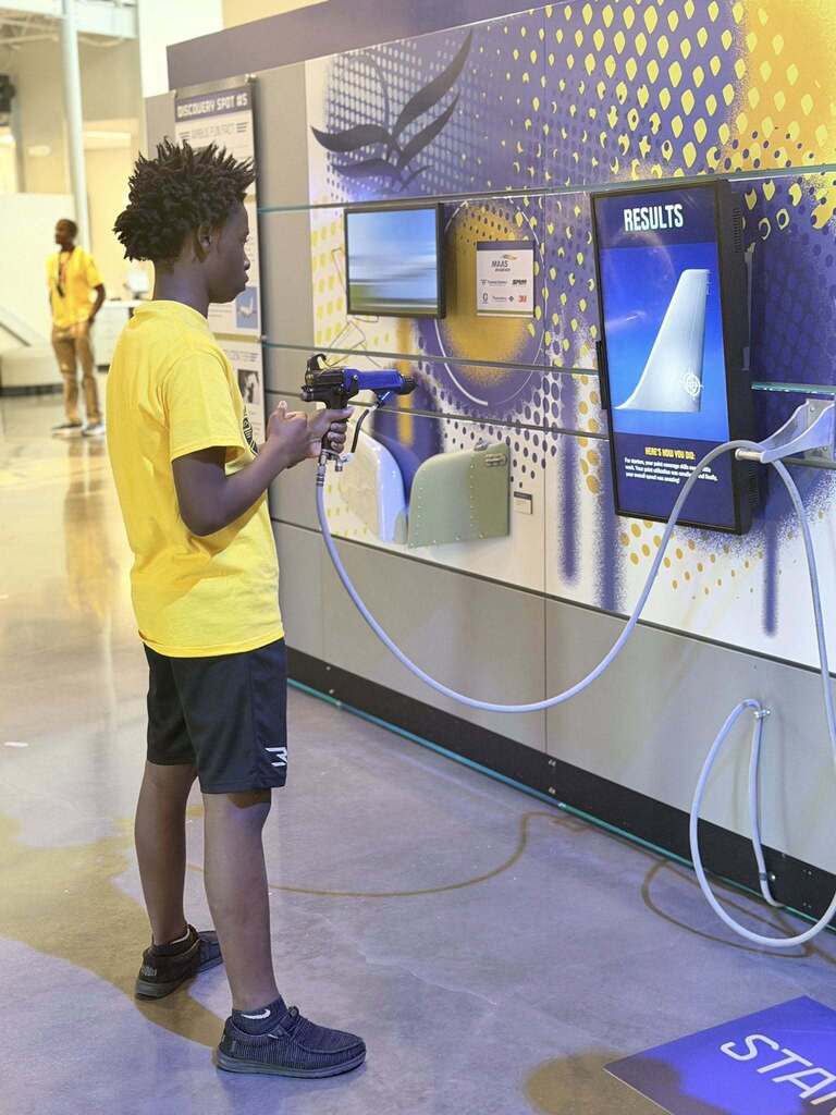 A student holds a paint sprayer at an interactive exhibit