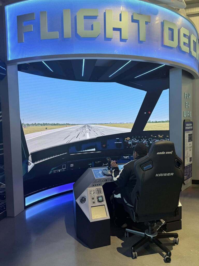 A student sits in a flight simulator, with a runway on the screen in front of him