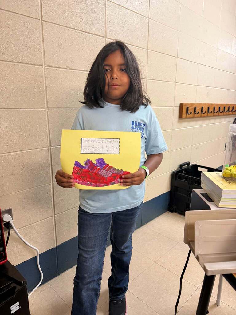 A girl holds her artwork of a shoe