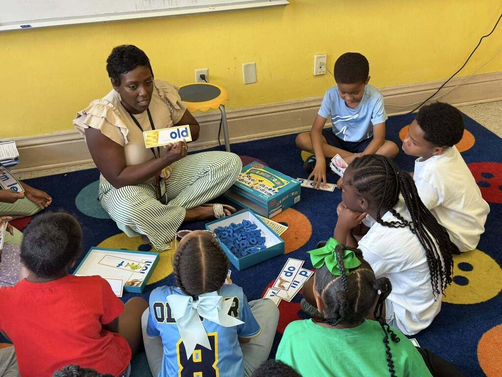 A teacher sitting on a rug, showing flashcards to a group of students