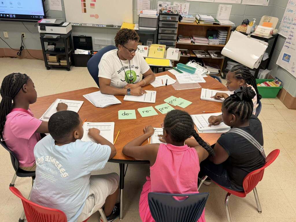 A teacher sits with students at a table, with flashcards of prefixes in front of them