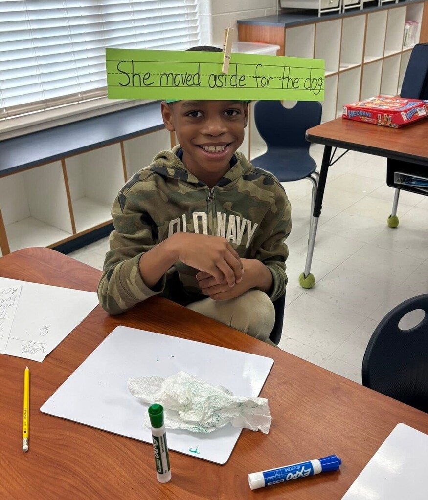 A student with a piece of paper with the sentence "She moved aside for the dog" attached to a headband on his head