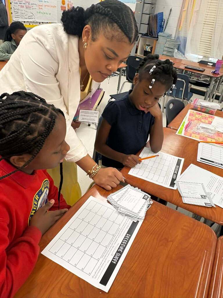 A teacher looks over to help two students working on worksheets
