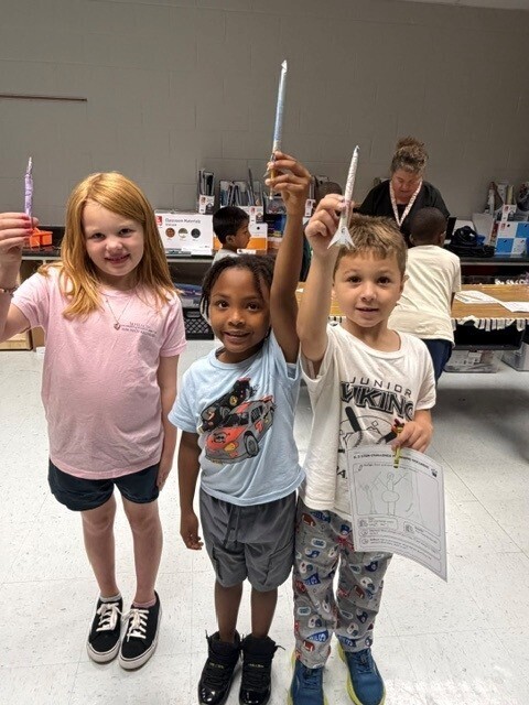 Three elementary students holding up straw rockets