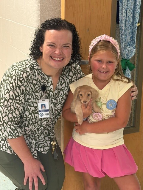 A teacher stands with a student who is holding a puppy
