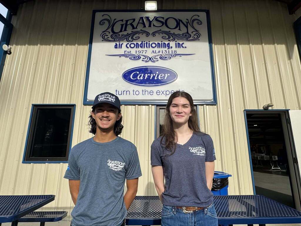 Two high school students standing outside an air-conditioning repair company