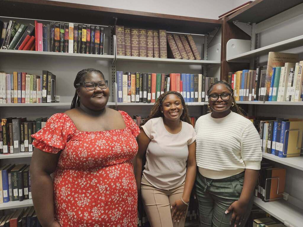 Three high school students standing in a library