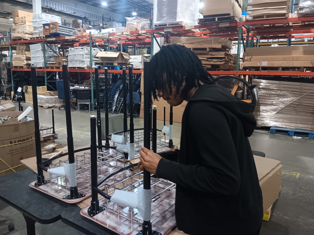 A high school student assembling small desks in a warehouse