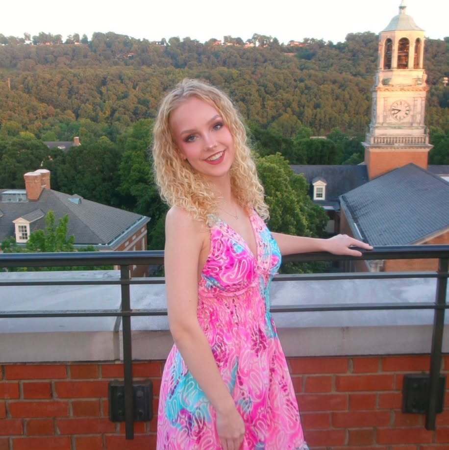 Katie Wilborn, wearing a pink dress and standing on a rooftop