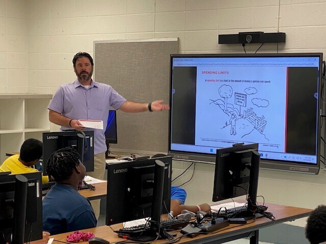 A man speaks in front of a classroom on elementary students
