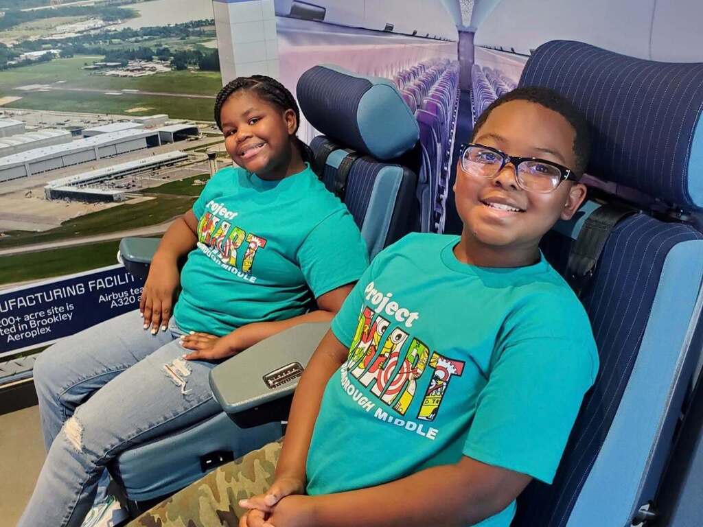 Two students sitting in models of airliner seats