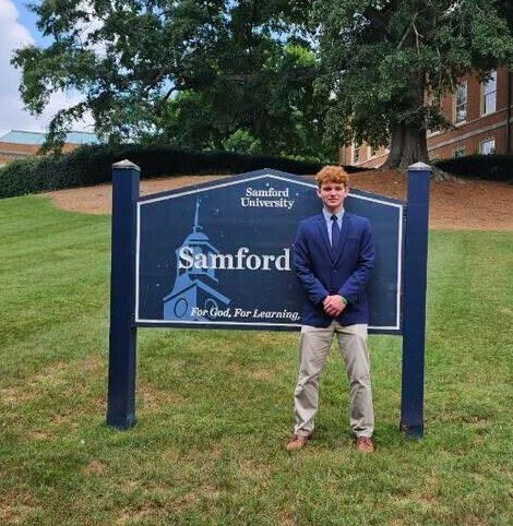 A boy in a blazer and tie standing in front of the Samford University sign