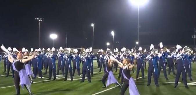 A high school marching band in blue uniforms  on a football field