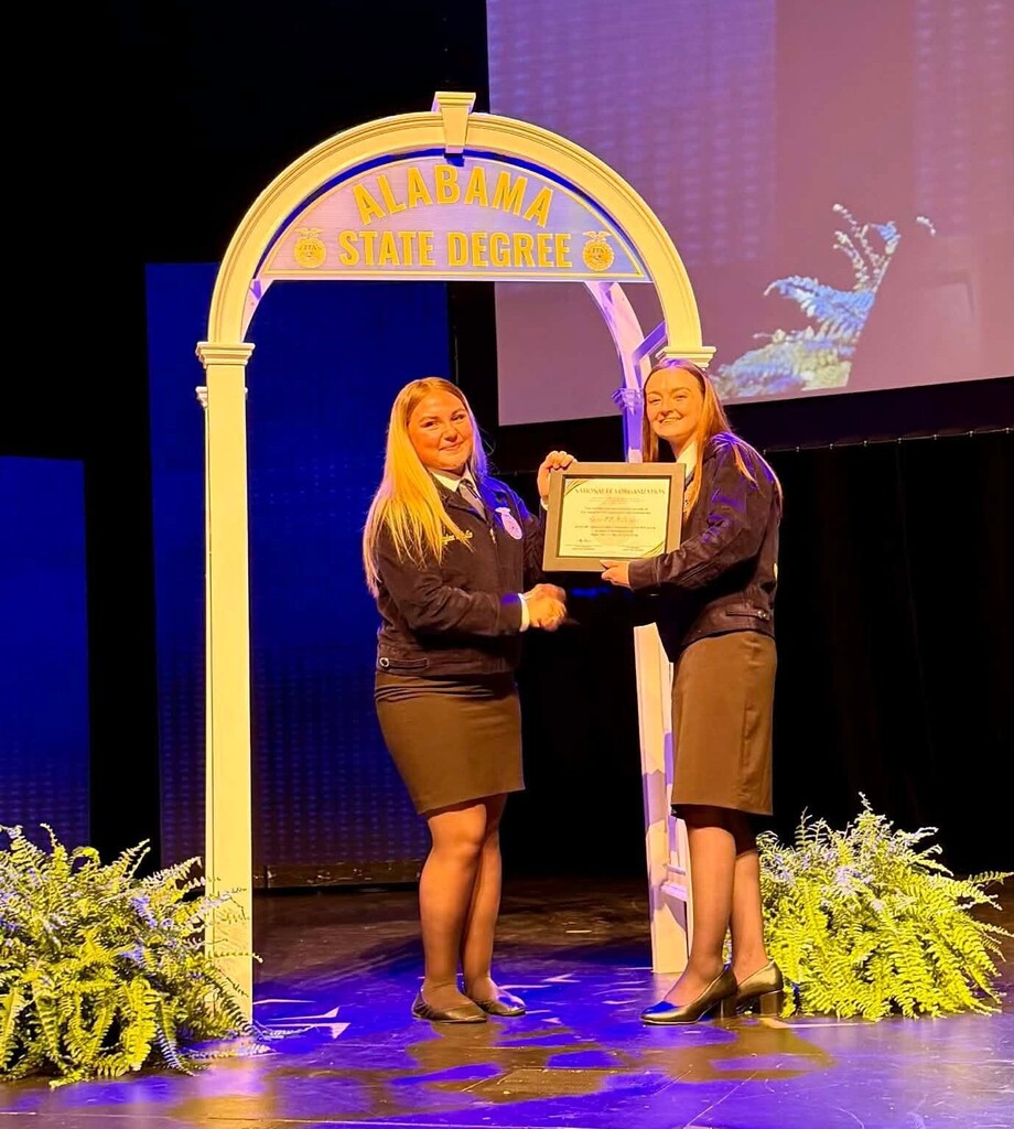 One girl handing a plaque to another on a stage