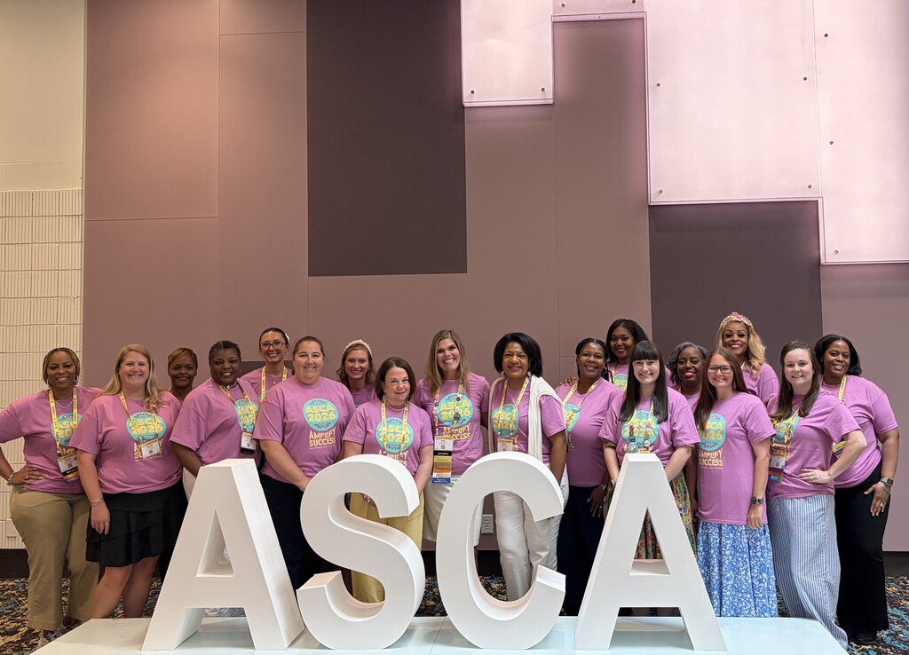 A group of counselors in pink T-shirts standing behind an ASCA sign