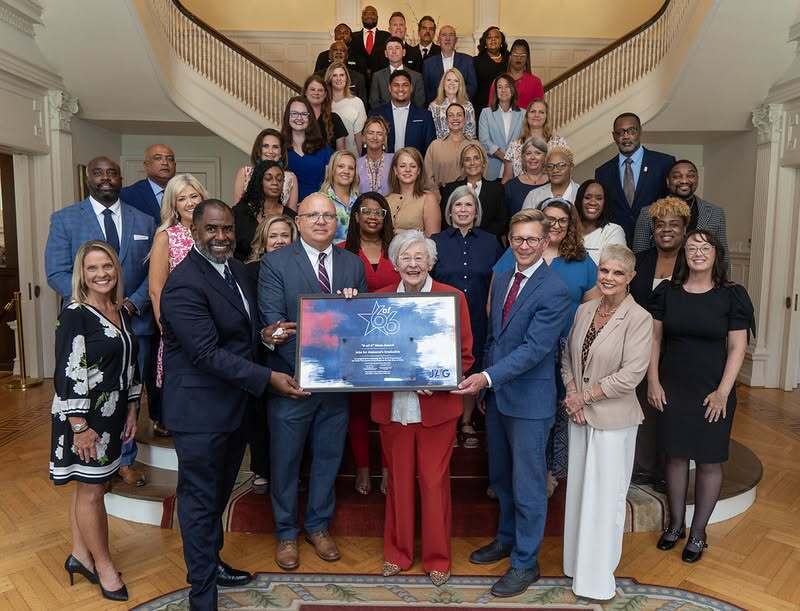 A large group of educators standing on a stairwell with Alabama Governor Kay Ivey
