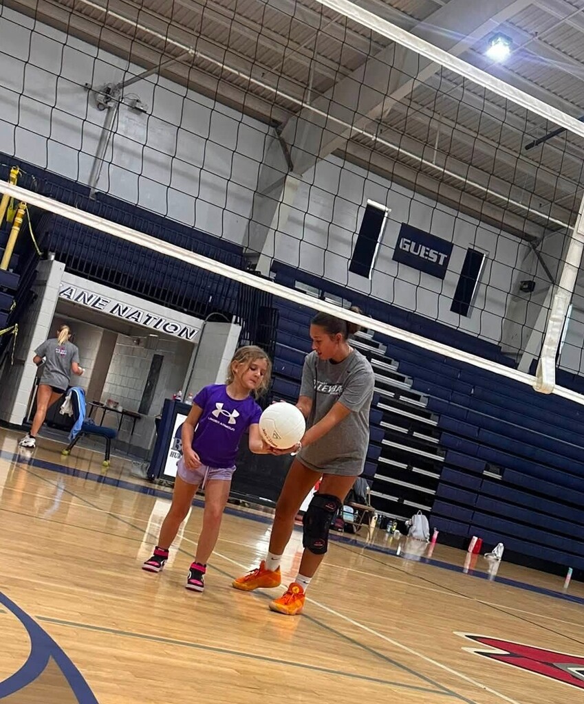 A high school girl showing an elementary girl how to serve a volleyball