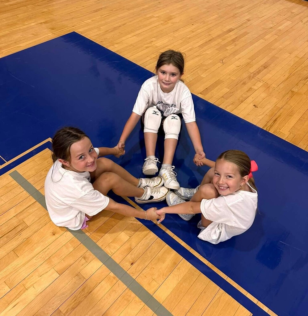 Three girls holding hands while sitting on a gymnasium floor