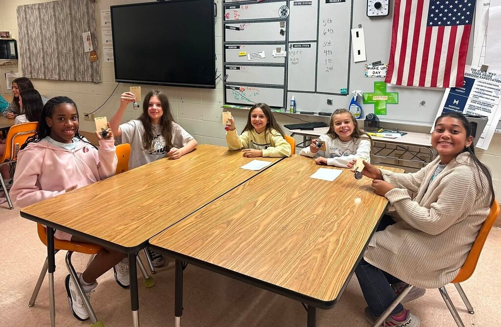 Five girls sitting around a table, holding up cards
