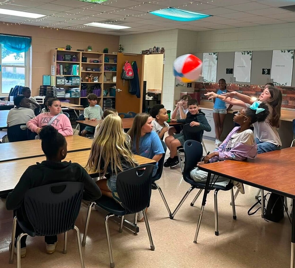 Students seated in a classroom, with one knocking a beach ball into the air