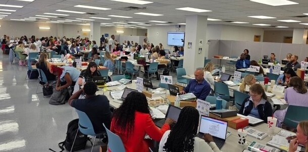 A large group of teachers sitting at tables with laptops in a big room