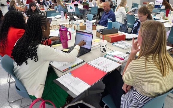 Teachers sitting at tables with laptops and notebooks