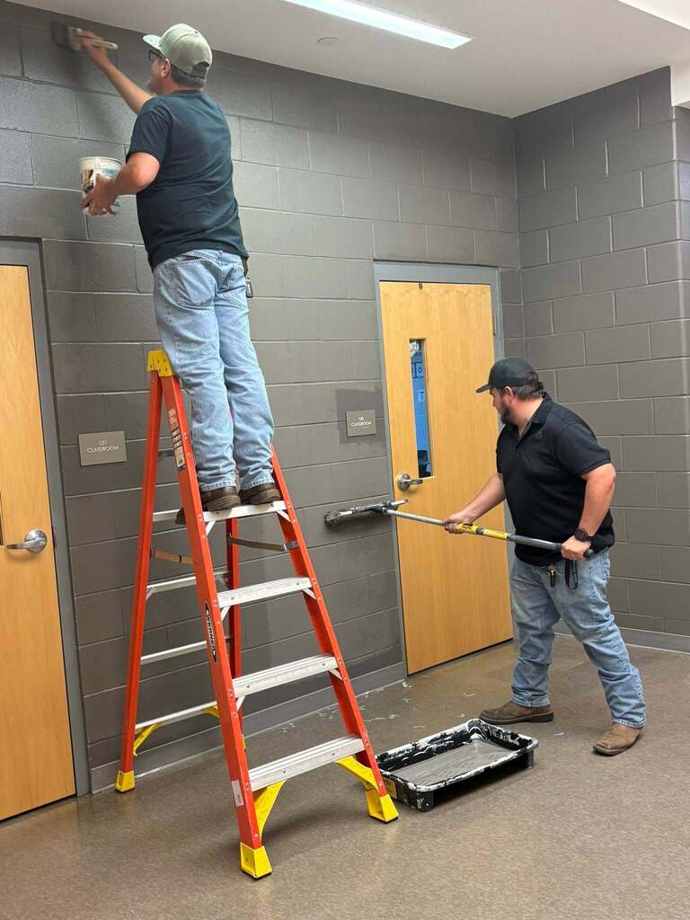 Two men painting the wall in a school hallway