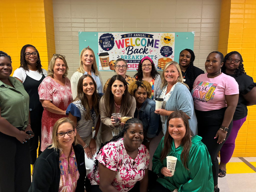 Teachers posing in front of Welcome Back banner