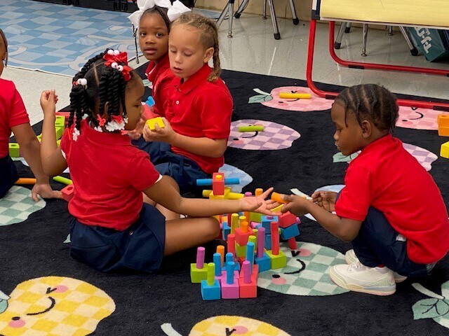 Students seated on a rug, building things with blocks