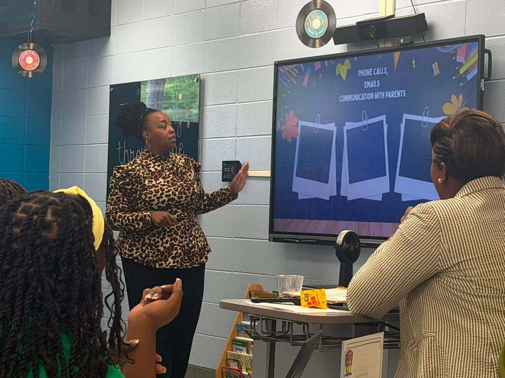 A teacher pointing at a smartboard while other teachers look on 