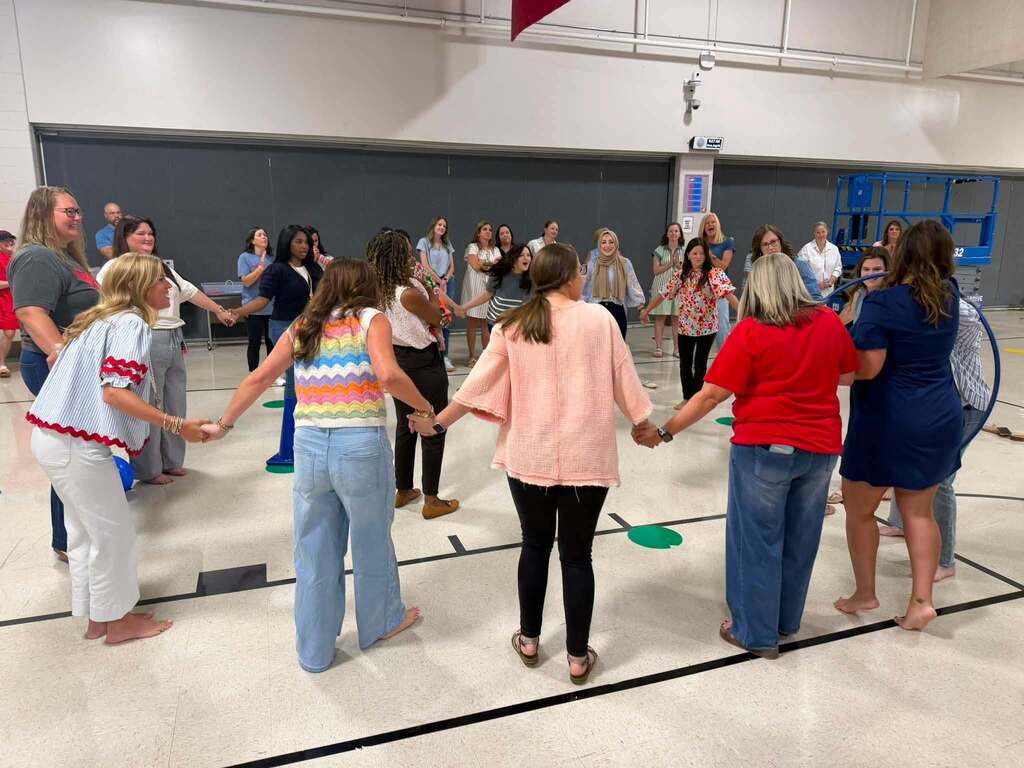 A group of teachers holding hands in a circle in a gymnasium