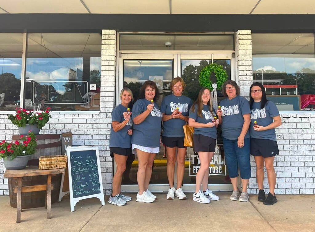 Six teachers standing outside a store, holding small jars of honey