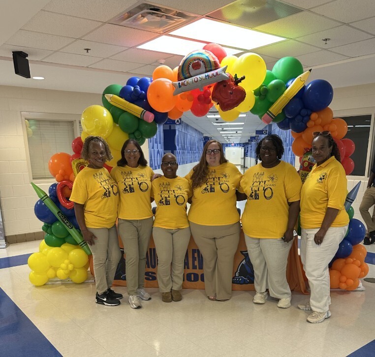 CTE staff group photo under the balloon arc in matching yellow shirts