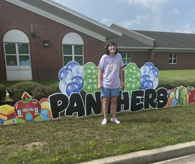 Student in front of panther sign in front of the school