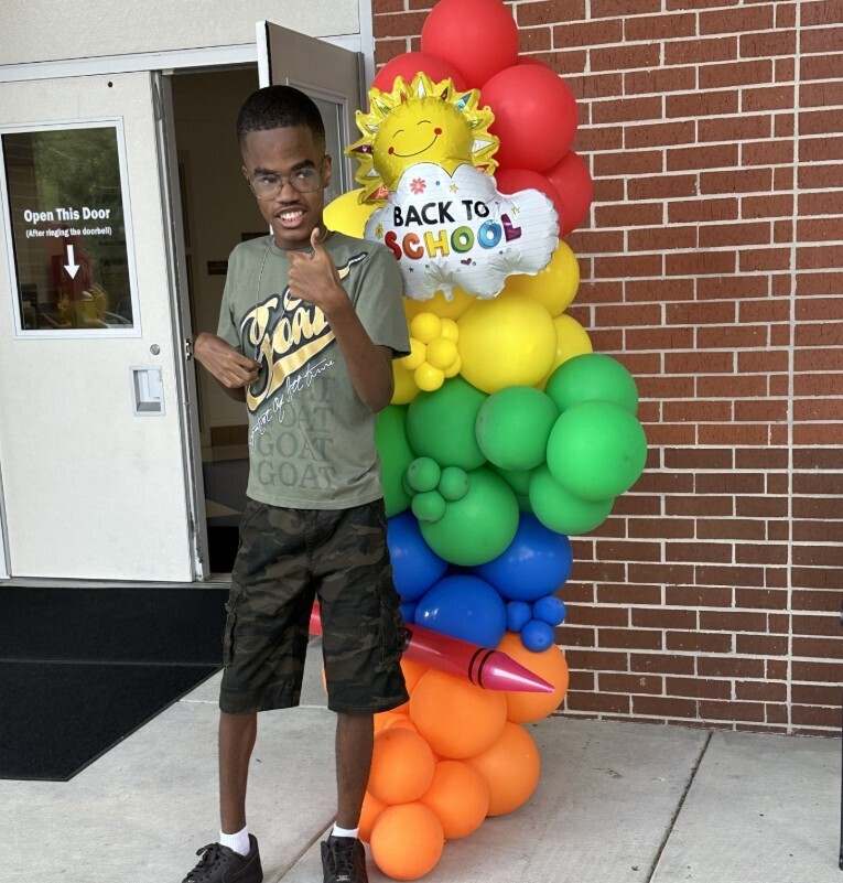 Student by balloon decorations giving a thumbs up
