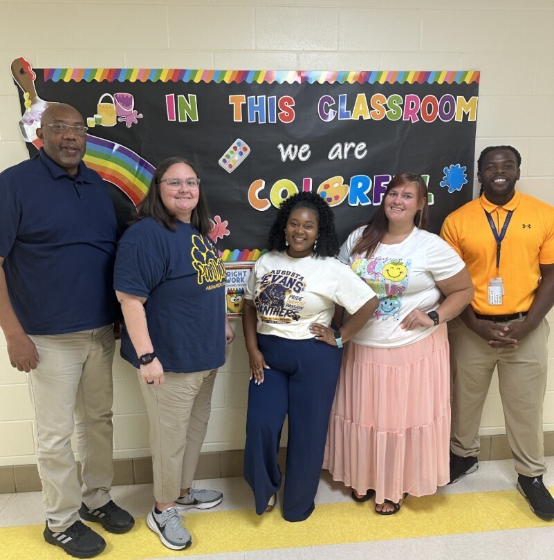 Rise level group staff photo in front of hallway classroom welcome sign