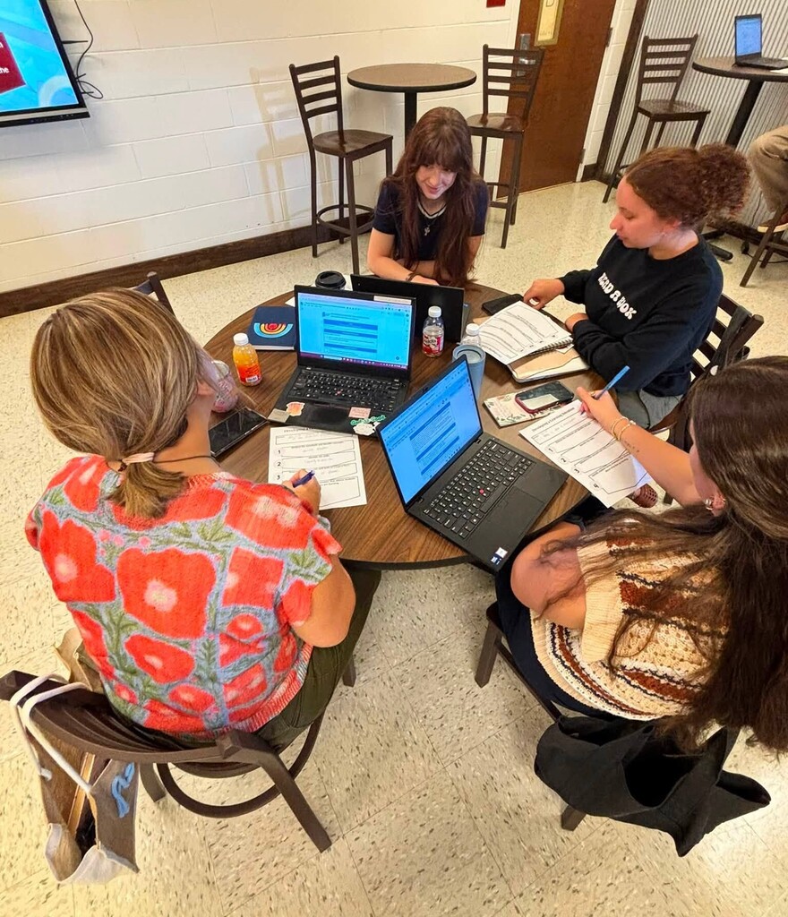 Teachers seated around a table, working at laptops