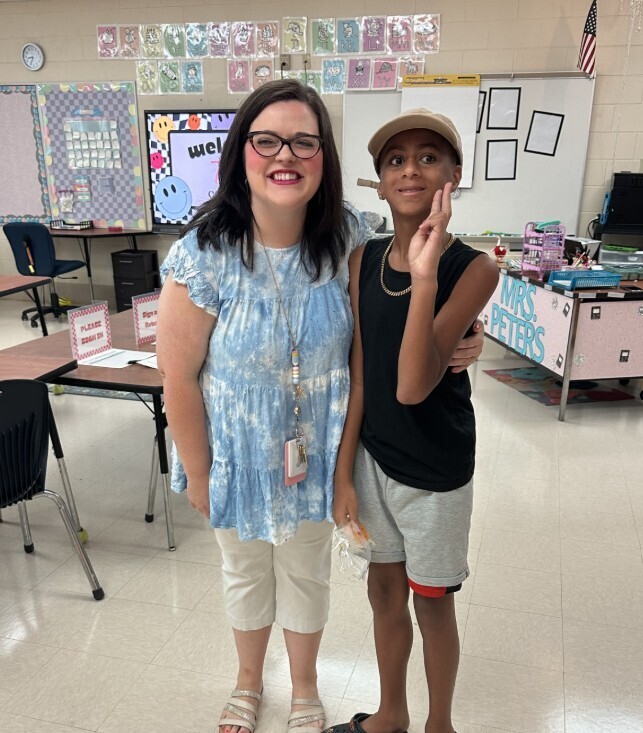 Leopard level teacher with student smiling and making a "peace" sign with hand in classroom for meet the teacher